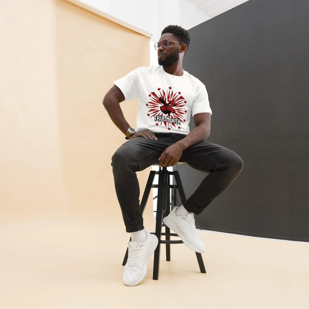 Man wearing white True North moose graphic tee, black jeans, white sneakers, sitting on stool